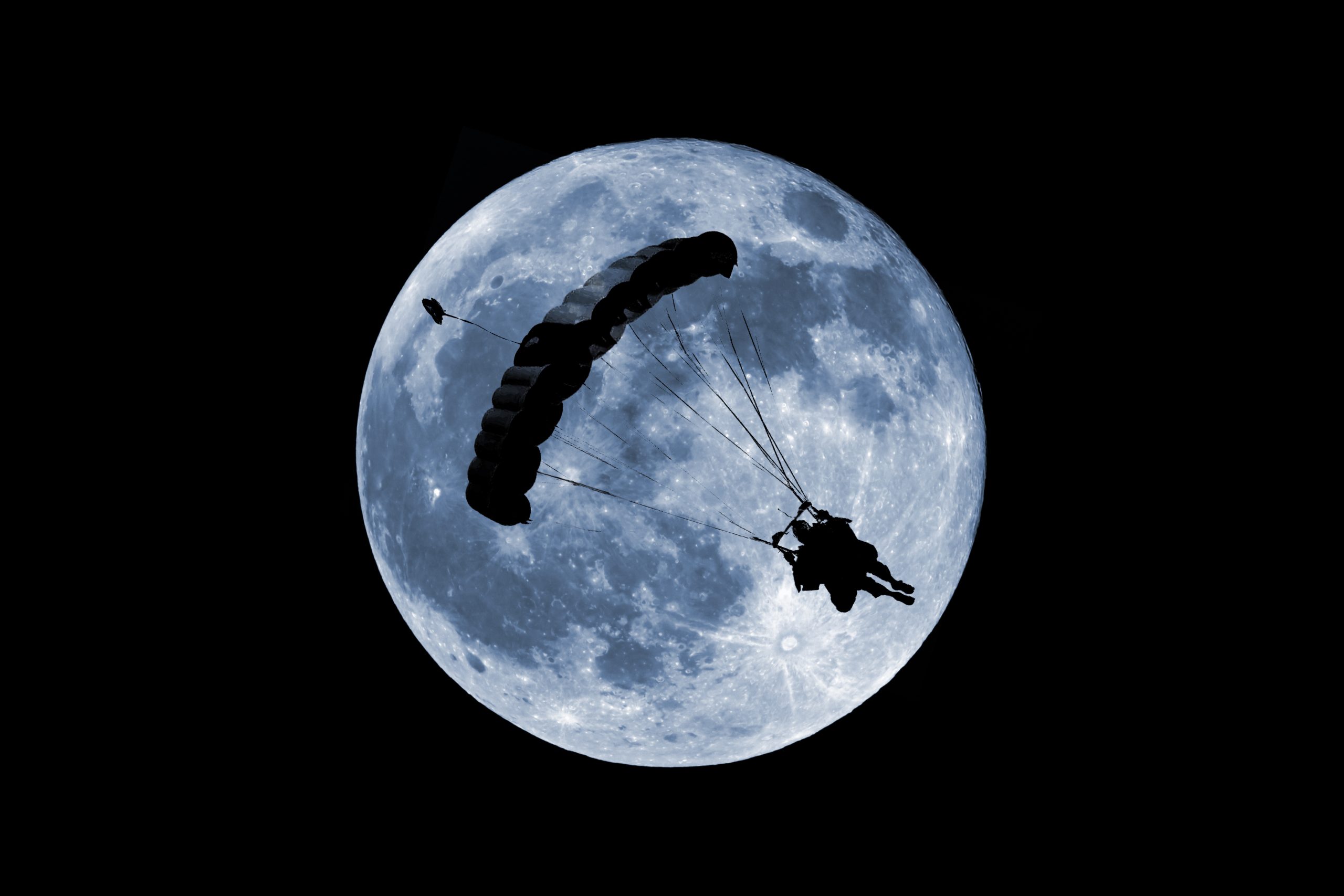 skydiver in front of the moon flying under their parachute at night