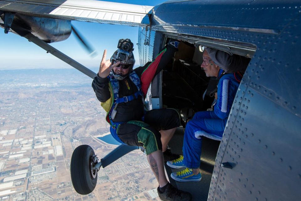A videographer hangs from the door of the Twin Otter in flight.