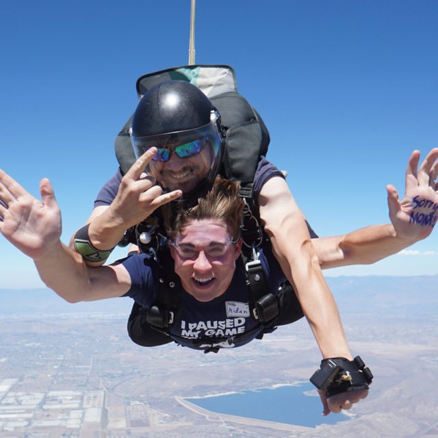 benefits of getting out of your comfort zone tandem skydivers smile in freefall and give the rock on hand symbol