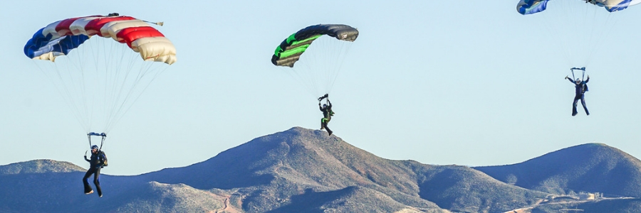 3 fun jumpers fly under canopy against backdrop of mountains