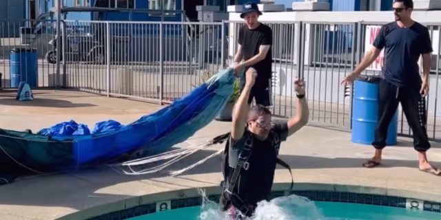 skydiver practices water training by jumping into a pool with a parachute