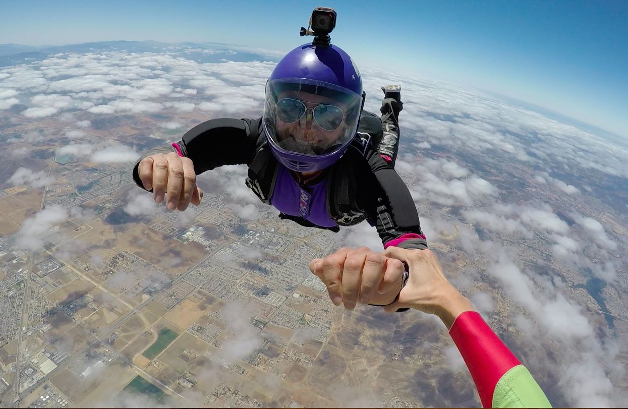 skydiver in purple helmet and camera smiles in freefall wearing aviator sunglasses
